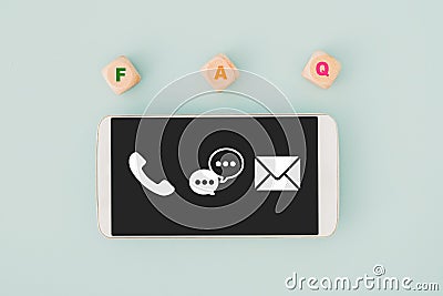 Smartphone with contact us icon on touchscreen with FAQ , Frequency Ask Question, on wooden cube block Stock Photo