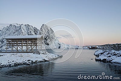 White snow cover mountain peak, coast, and cod fish wooden rack in Lofoten Islands Norway with cotton candy sky in winter Stock Photo