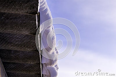 White snow and icicles hanging from the slate roof against the blue sky Stock Photo