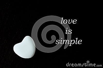 White stone heart on black background with the words `love is simple`. Stock Photo