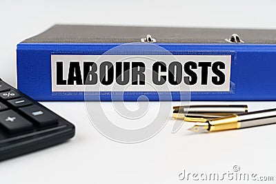 On a white surface, a calculator, a pen and a folder with the inscription - LABOUR COSTS Stock Photo