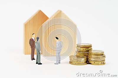 On a white surface stand wooden houses, coins and miniature figurines of businessmen negotiating a sale. Stock Photo