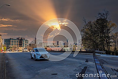 A white SUV driving over a freeway overpass in the city with skyscrapers and office buildings in the city skyline Editorial Stock Photo