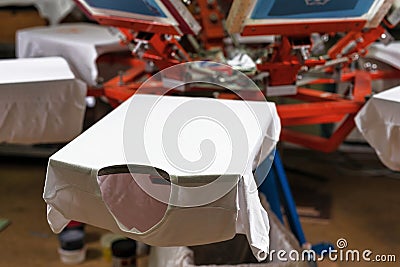 A white t-shirt on wooden shelve of the print screening apparatus. serigraphy production. printing images on t-shirts Stock Photo