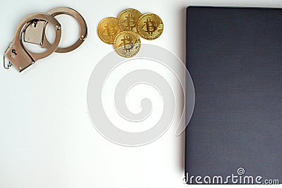 On a white table, the edge of a gray laptop, handcuffs and bitcoin coins. Near a copy space. Cybercrime concept Stock Photo