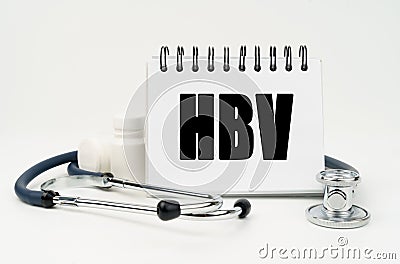 On a white table lies a stethoscope, pills and a notebook with the inscription - HBV Stock Photo