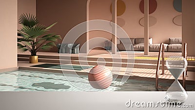 White table or shelf with crystal hourglass measuring the passing time over colored contemporary living room, pastel rosy colors, Stock Photo