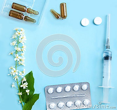 White tablets, glass ampoules, a syringe and cherry blossoms are arranged on a light blue background. Stock Photo