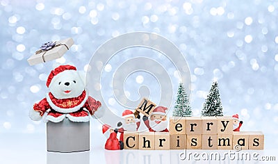 White teddy bear emerges from gift box with Santa Claus dolls are sorting Merry Christmas wooden cubes for on snowing background Stock Photo