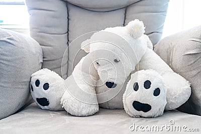 White teddy bear slouching on a plush grey nursery chair. Backlit with natural sunlight Stock Photo