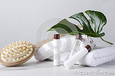 White towels, wooden brush for massage, bottles of lotion, body cream, green tropical leaf as a decor on the white table against b Stock Photo
