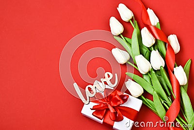 White tulips, gift box with wooden letters LOVE on a red background. Stock Photo