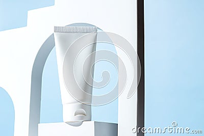 White unbranded plastic squeeze tube for cream or shampoo stands on white podium in white arch on blue background Stock Photo