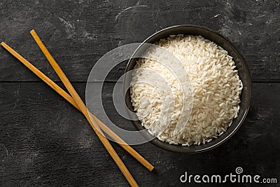 White uncooked, raw long grain rice in black bowl on rustic, dark wooden table top view flat lay from above Stock Photo