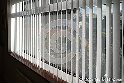 White vertical blinds slats hanging in front of double glazed white frame window. The slats have no cords at the bottom. Stock Photo