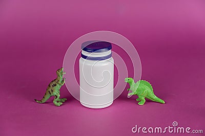 White vial and dinosaur miniatures against a purple background. Small green figures of predatory animals standing on their hind Stock Photo