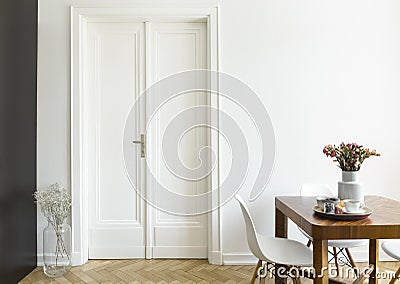 A white wall with double door next to a wooden breakfast table and chairs in a dining room interior. Real photo. Stock Photo