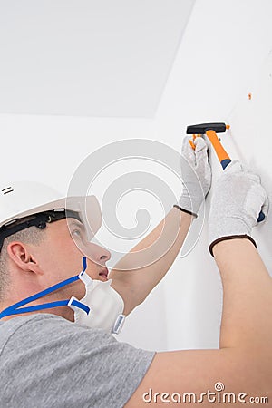 In a white wall, holes are made and orange dowels are hammered with a hammer, a master in a protective helmet Stock Photo