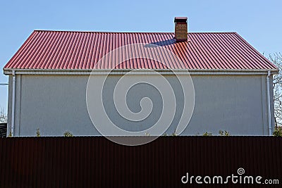 White wall of a house with a red roof behind a brown fence Stock Photo