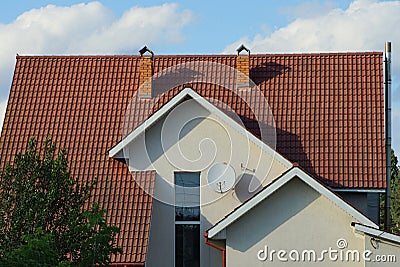 White wall of a private house with windows under a red tiled roof with chimneys Stock Photo