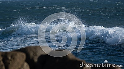 White wave on ocean surface, on a blustery, windy day with rocks in foreground. Stock Photo