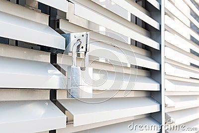 White wavy metal door of an industrial building with locked padllock during quarantine.solar reflections.Outdoor shoot Stock Photo