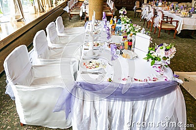 White wedding party table with fancy chairs and a lot of flowers, decorations, beverages and plates with food Stock Photo