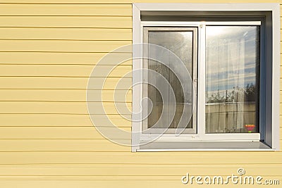 White window on the wall lined with yellow siding Stock Photo