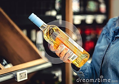 White wine bottle in hand in liquor store. Customer buying alcohol. Woman choosing the right bottle of chardonnay or riesling. Stock Photo