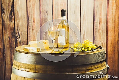 White wine in glass, bottle, grape and cheese on barrel front wood background. Stock Photo