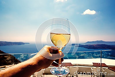 A white wine glass in hand against the backdrop of the Aegean sea and caldera on Santorini island. Stock Photo