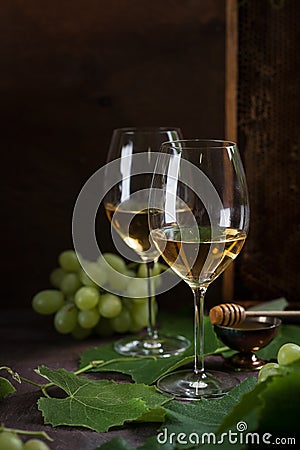 White wine in glasses. Glasses stand on a dark table next to the grape leaves and green grapes. Honeycombs stand in the background Stock Photo