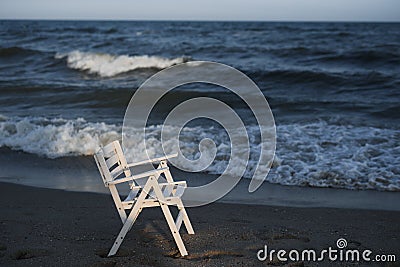 White wooden chair on the beach. Empty beach, sunset, cold weather and the sea. Stock Photo