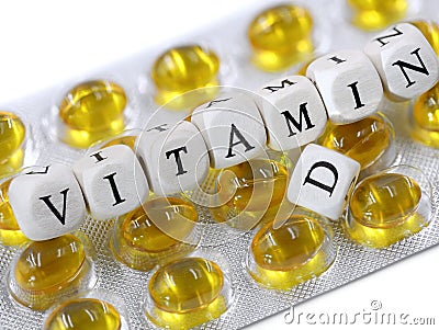 white wooden cubes with black letters form the text Vitamin D on yellow pill blister Stock Photo