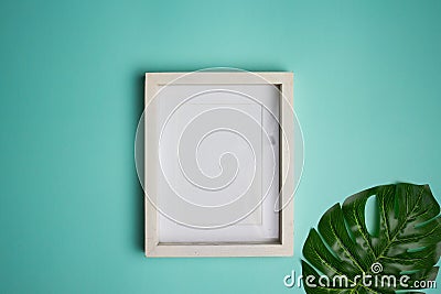 A white wooden frame with green leave over the mint background. Stock Photo