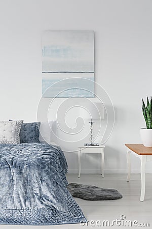 White wooden table with stylish lamp next to comfortable ned with blue pillows and duvet, real photo Stock Photo