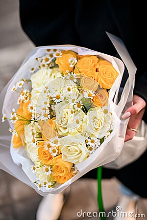 White and yellow roses and daisies in the hands of a girl in a black jacket Stock Photo