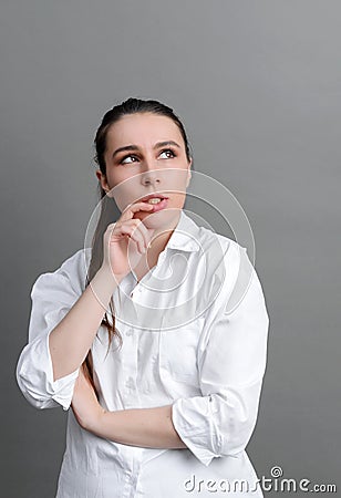 White young woman in a white shirt pondered against a gray Stock Photo