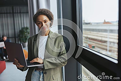 A whitecollar worker in formal wear holds a laptop by a window at a building Stock Photo