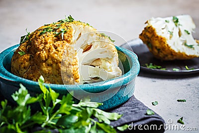 Whole baked cauliflower with spices and herbs in blue dish Stock Photo