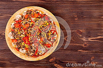 A whole delicious pizza with mushrooms, corn, cherry tomatos, courgettes and bell peppers on a round wooden plate Stock Photo