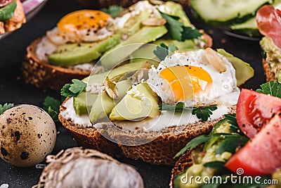 Whole grain bread sandwiches with fried quail egg, avocado, herbs and seeds on black background. Stock Photo