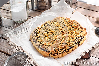 Whole grated pie on a sheet of parchment paper surrounded by kitchen utensils on a wooden table Stock Photo