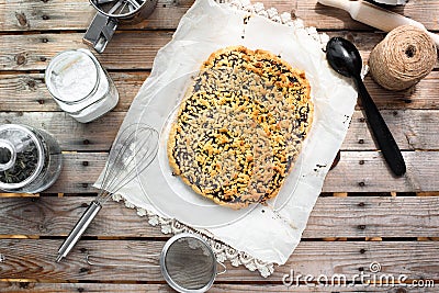 Whole grated pie on a sheet of parchment paper surrounded by kitchen utensils on a wooden table Stock Photo