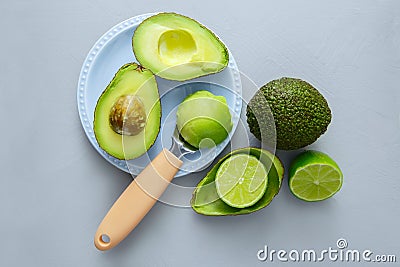 Whole and half avocado on a saucer, with a spoonful of pulp and fresh halves of green lime Stock Photo