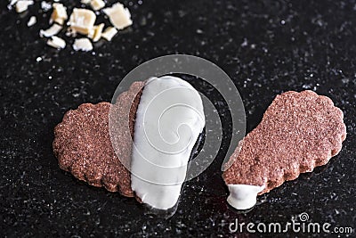 Whole heart shaped chocolate cookie with a broken heart shaped brown cookie on a black marble counter, close up Stock Photo