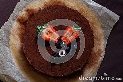 Whole homemade cheesecake on baking paper with cocoa and fruit topping from above Stock Photo