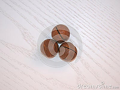 Whole macadamia nuts on a light wooden background. Macadamia nuts close-up. As many as three round macadamia nuts on a wooden surf Stock Photo