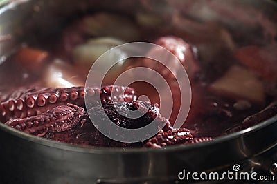 Whole octopus boiling in the the pot filled with water and vegetables. Tentacles of red octopus being boiled. Stock Photo