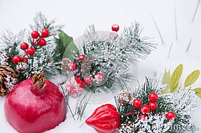 Whole pomegranate fruit and green spruce branches with cone, berries in fresh snow, Christmas Stock Photo